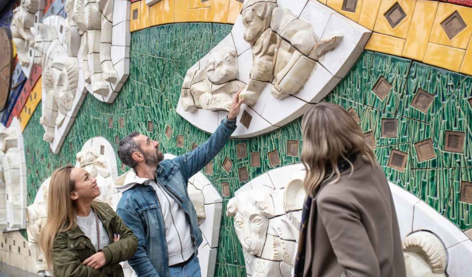 Three people observing a mosaic wall with animal sculptures in Tokyo