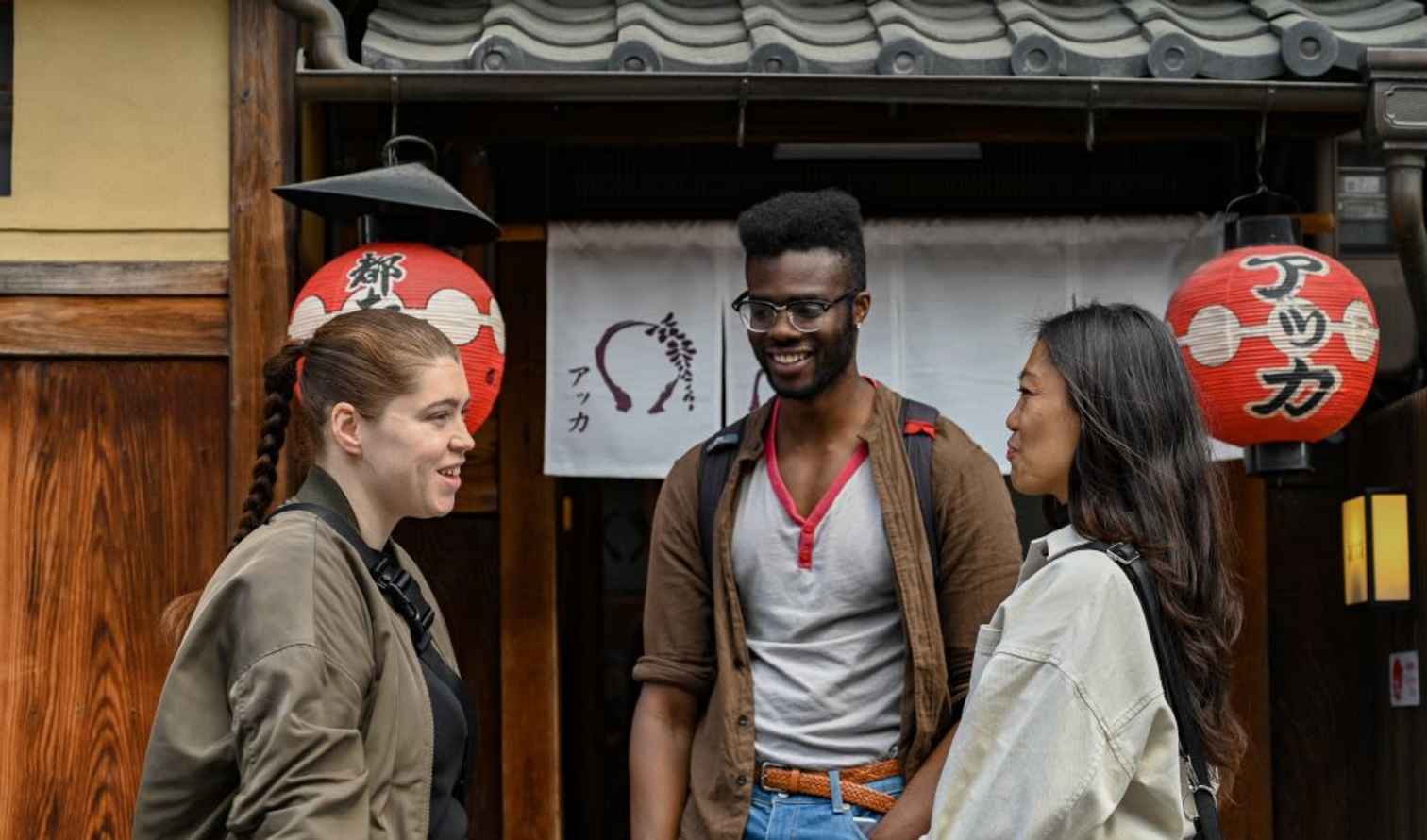 Three people stand outside a Japanese restaurant with red lanterns in Kyoto