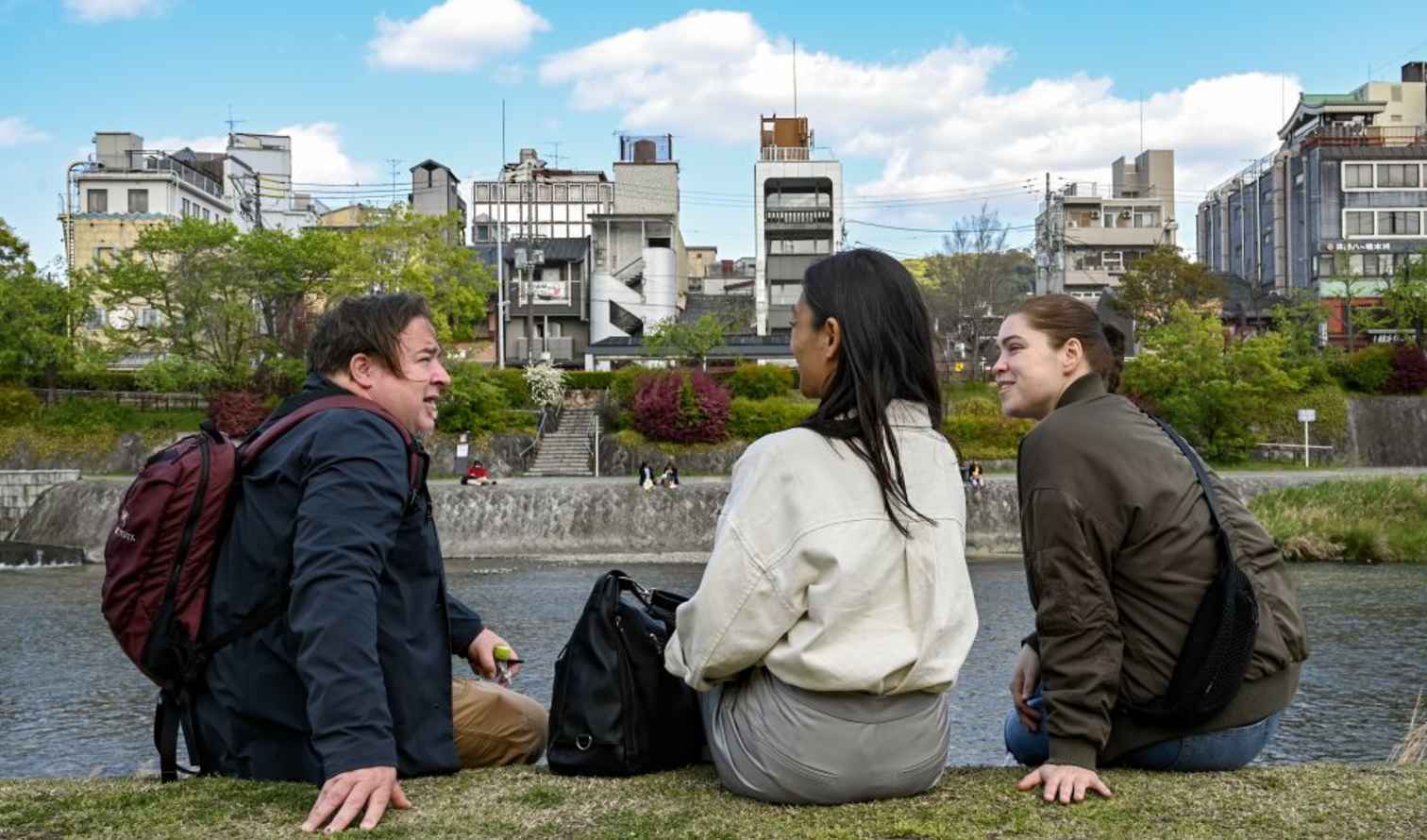 Three people sitting by the Kamo River in Kyoto, Japan.