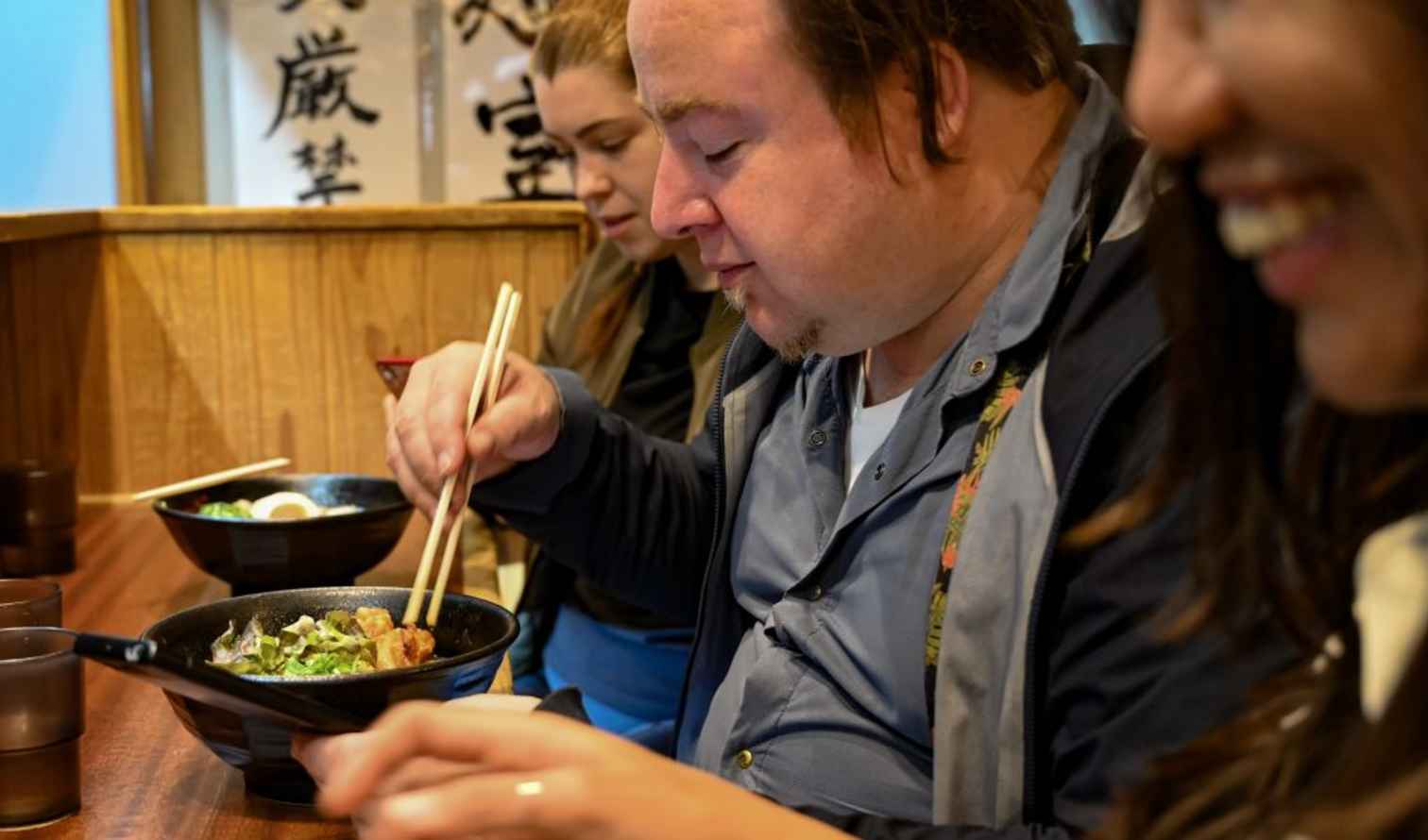 Three people eating ramen at a wooden counter in a restaurant in Kyoto