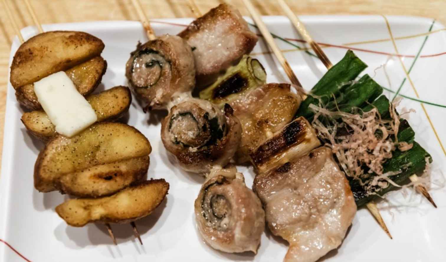 Grilled skewers of meat, vegetables, and potatoes on a white plate in Kyoto