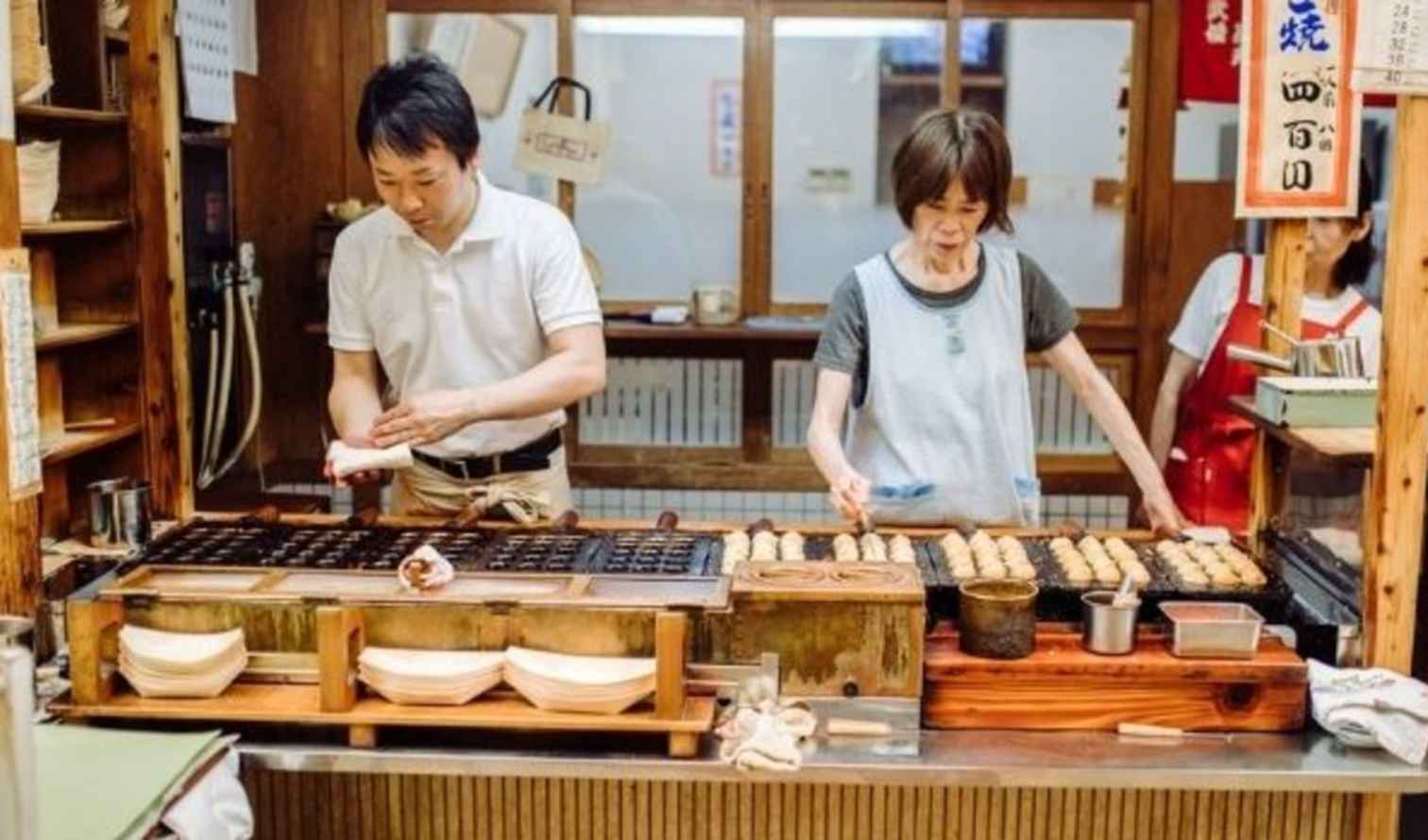 People cooking takoyaki in a Japanese street food stall in Osaka