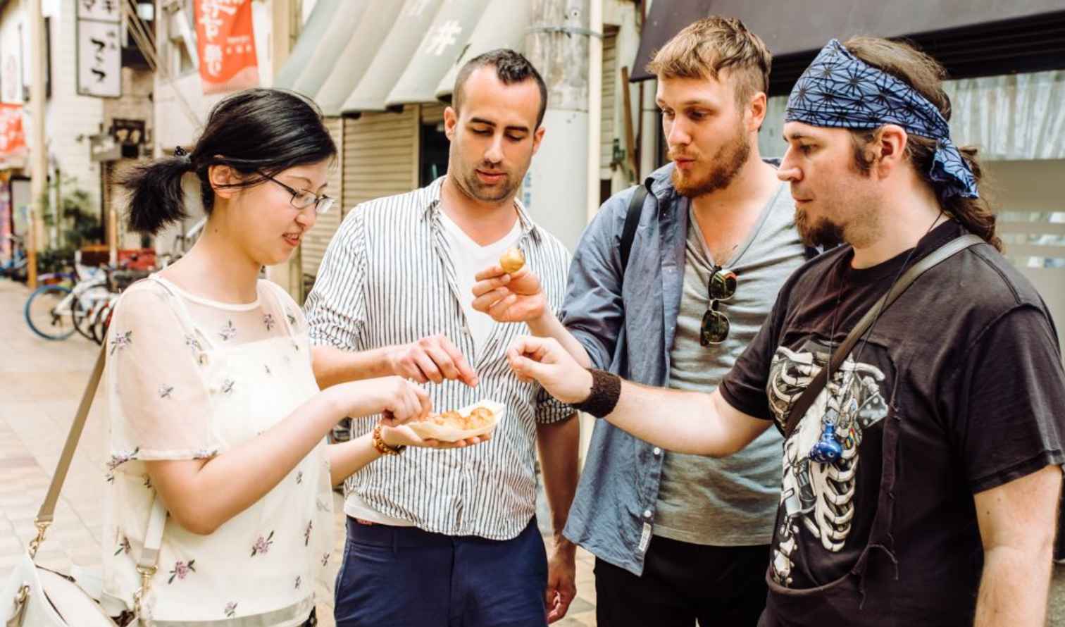 Four people sharing snacks on a street in Osaka