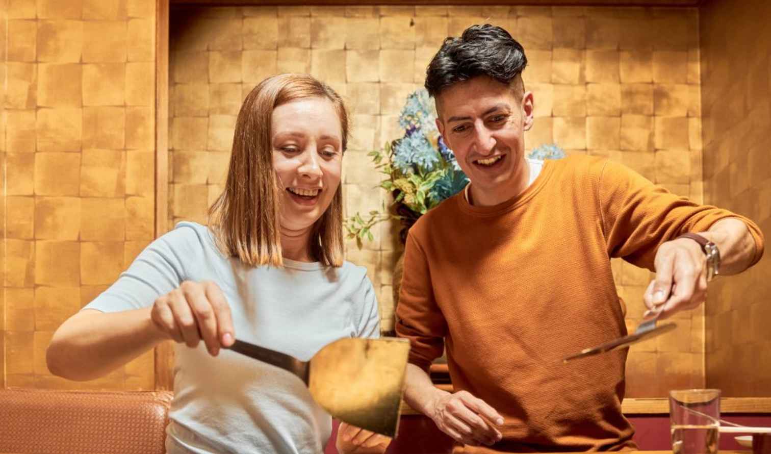 Two people serving food indoors with golden wall backdrop in Osaka