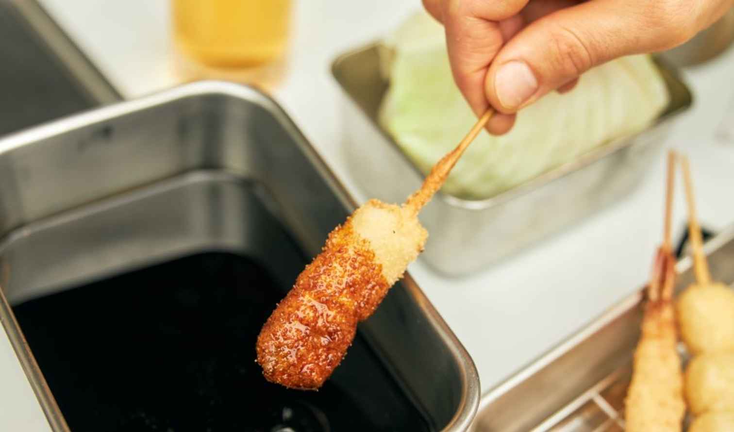 A hand dipping a skewered fried item into a sauce in Osaka