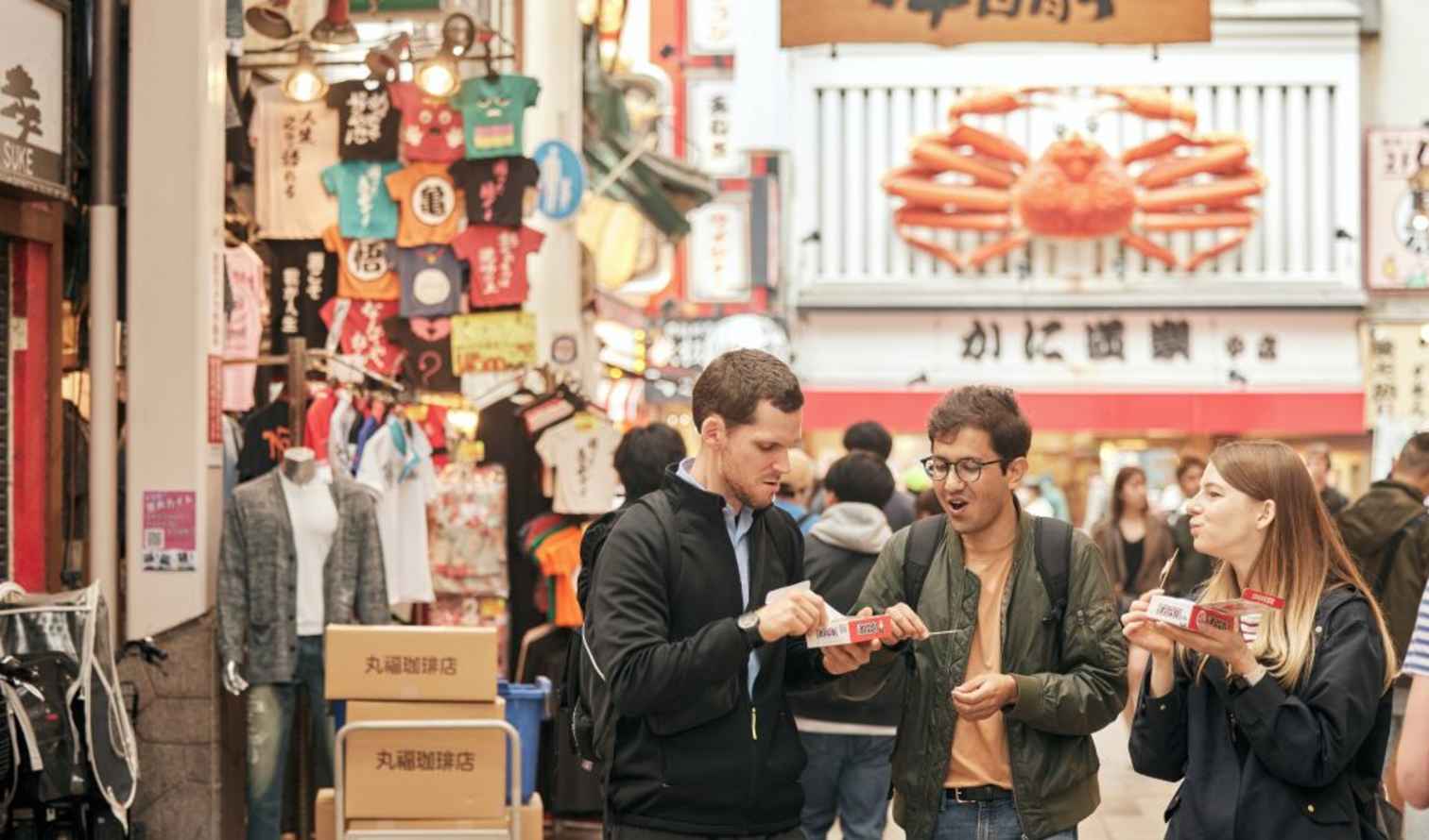 People eating on Dotonbori Street in Osaka, Japan, near a store with a crab sign.