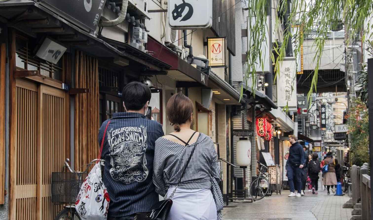 Two people walking on a Japanese shopping street with traditional signs in Osaka