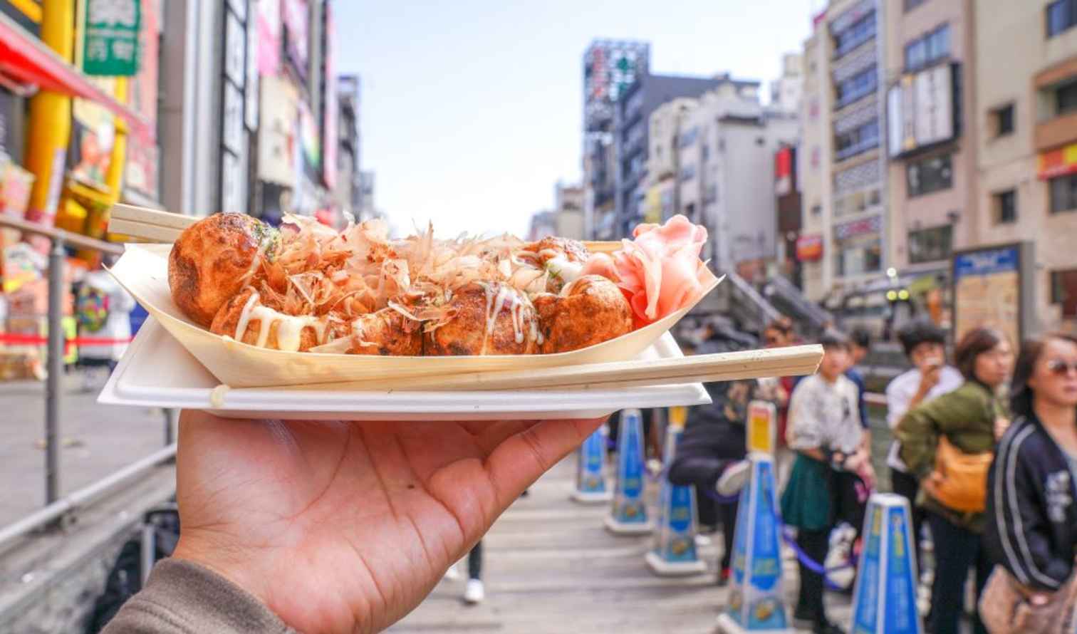 Takoyaki held up against a busy street in Dotonbori, Osaka.