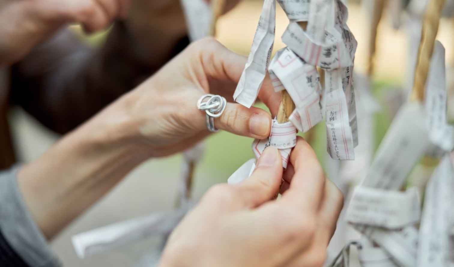 Hands tying paper fortunes at a Japanese shrine in Osaka