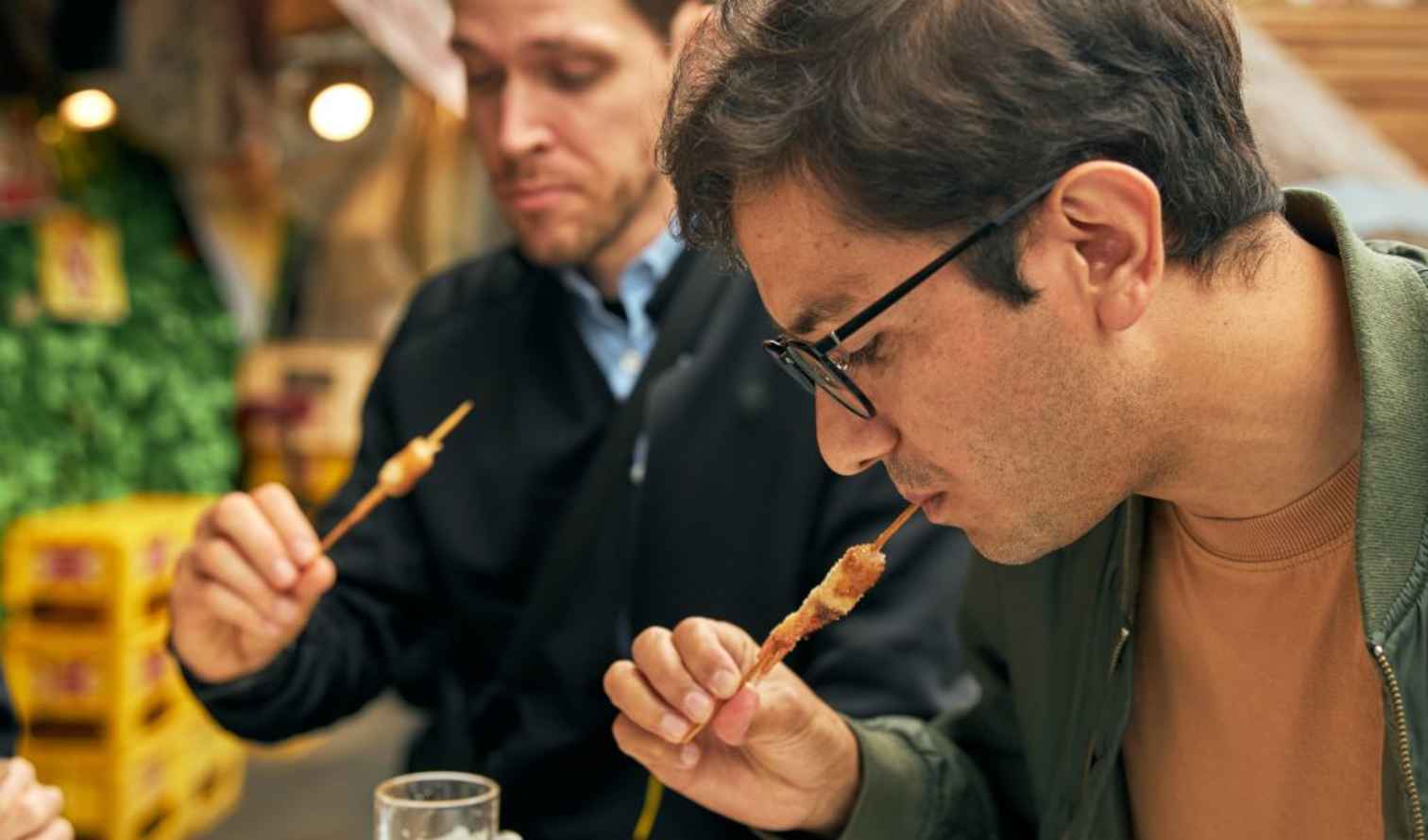 Two people eating skewers at an outdoor market in Osaka