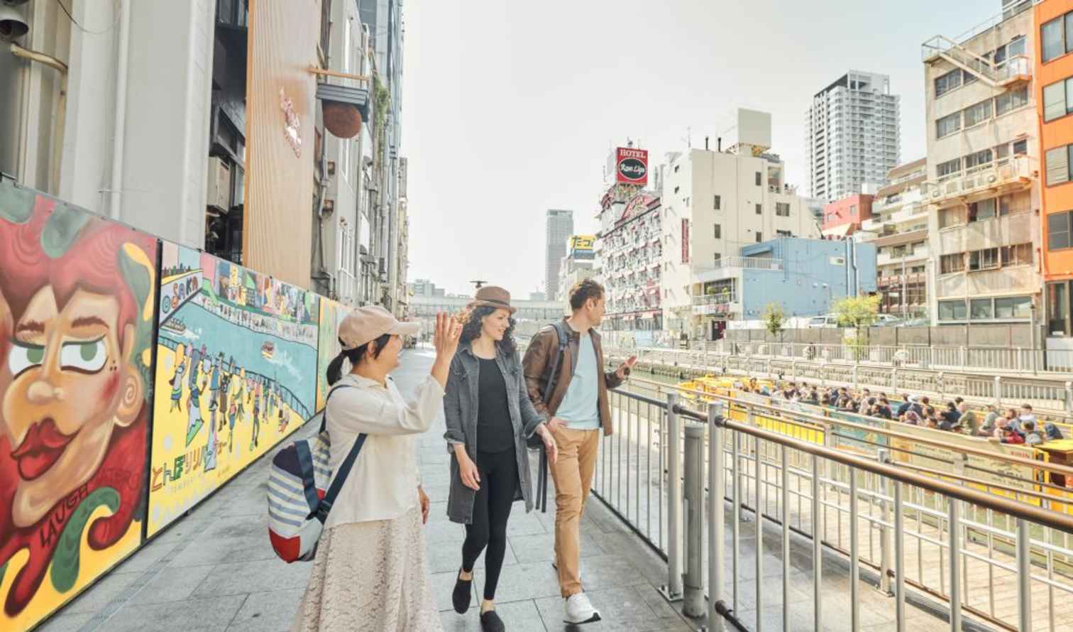 Three people walk along Dotonbori Canal in Osaka, Japan.