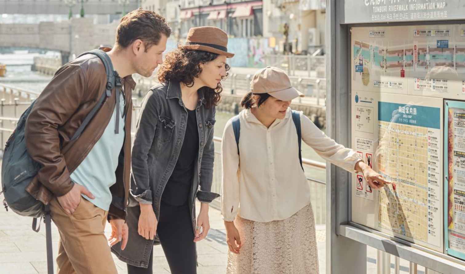 Three people examine a map on the Tombori Riverwalk in Osaka, Japan.