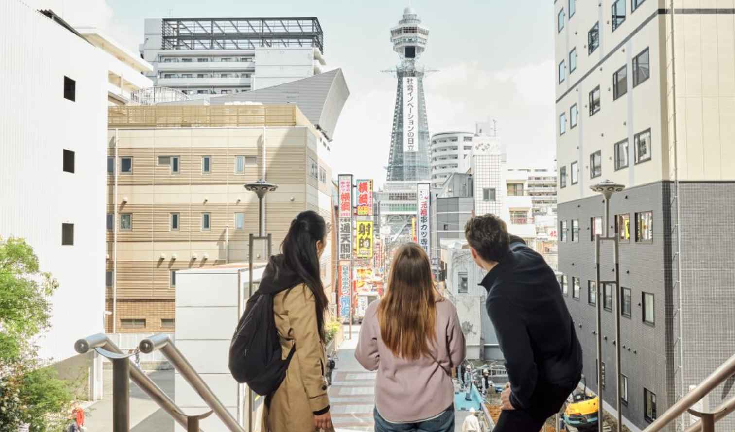 Three people looking at Tsutenkaku Tower in Osaka, Japan.