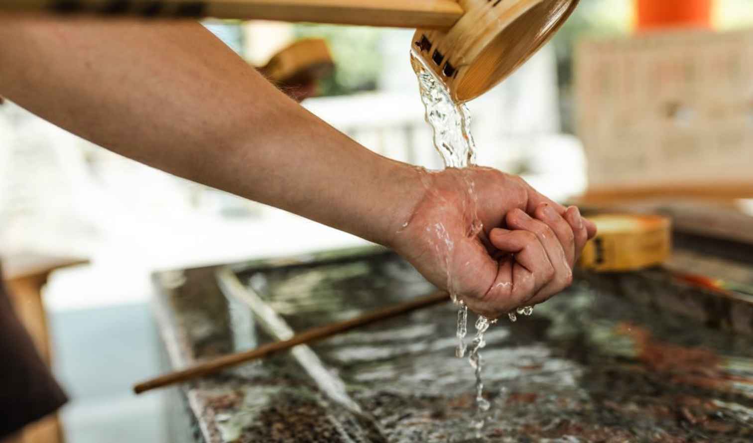 Person using a wooden ladle to pour water over their hand in Osaka