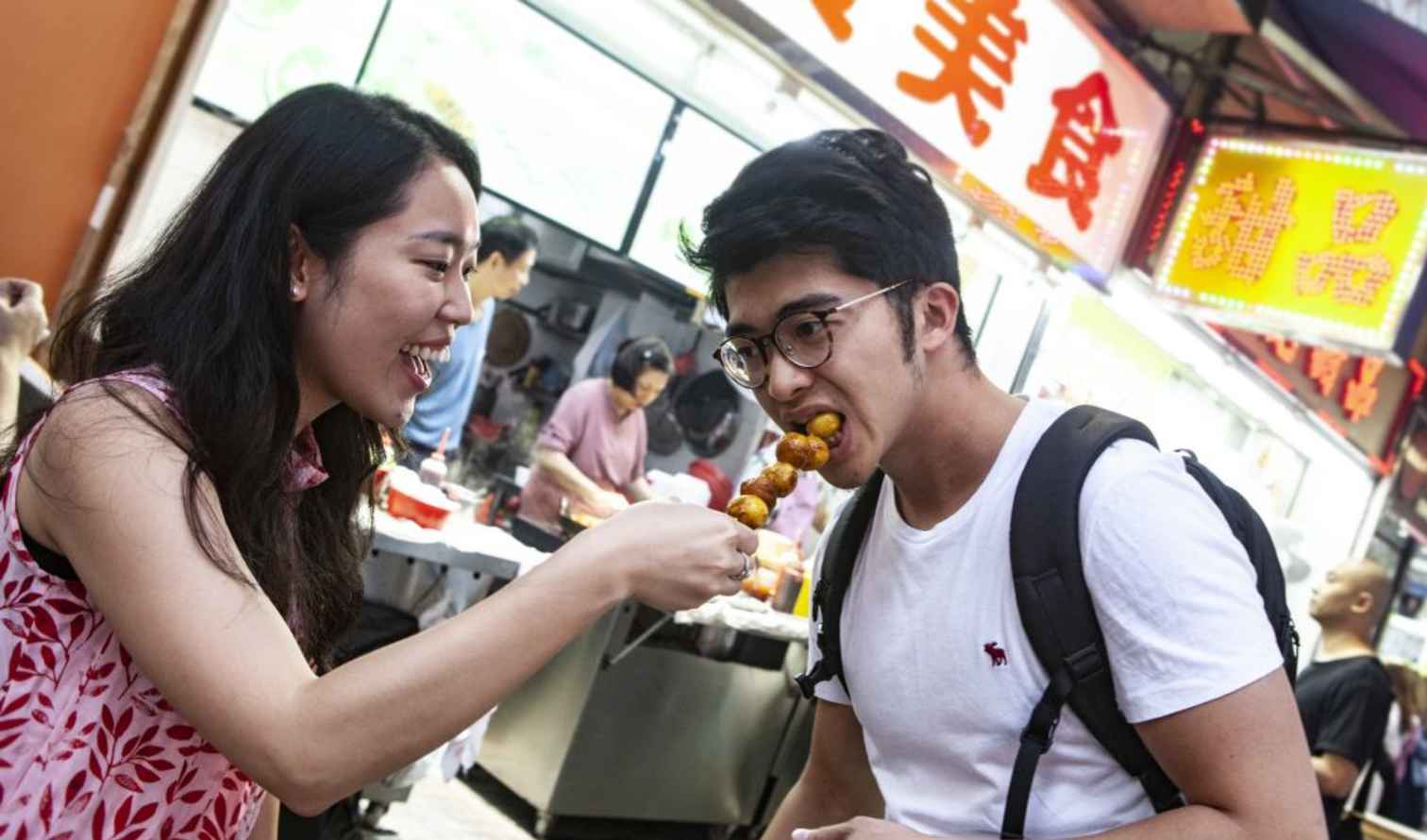 Two people sharing street food in a Hong Kong market.