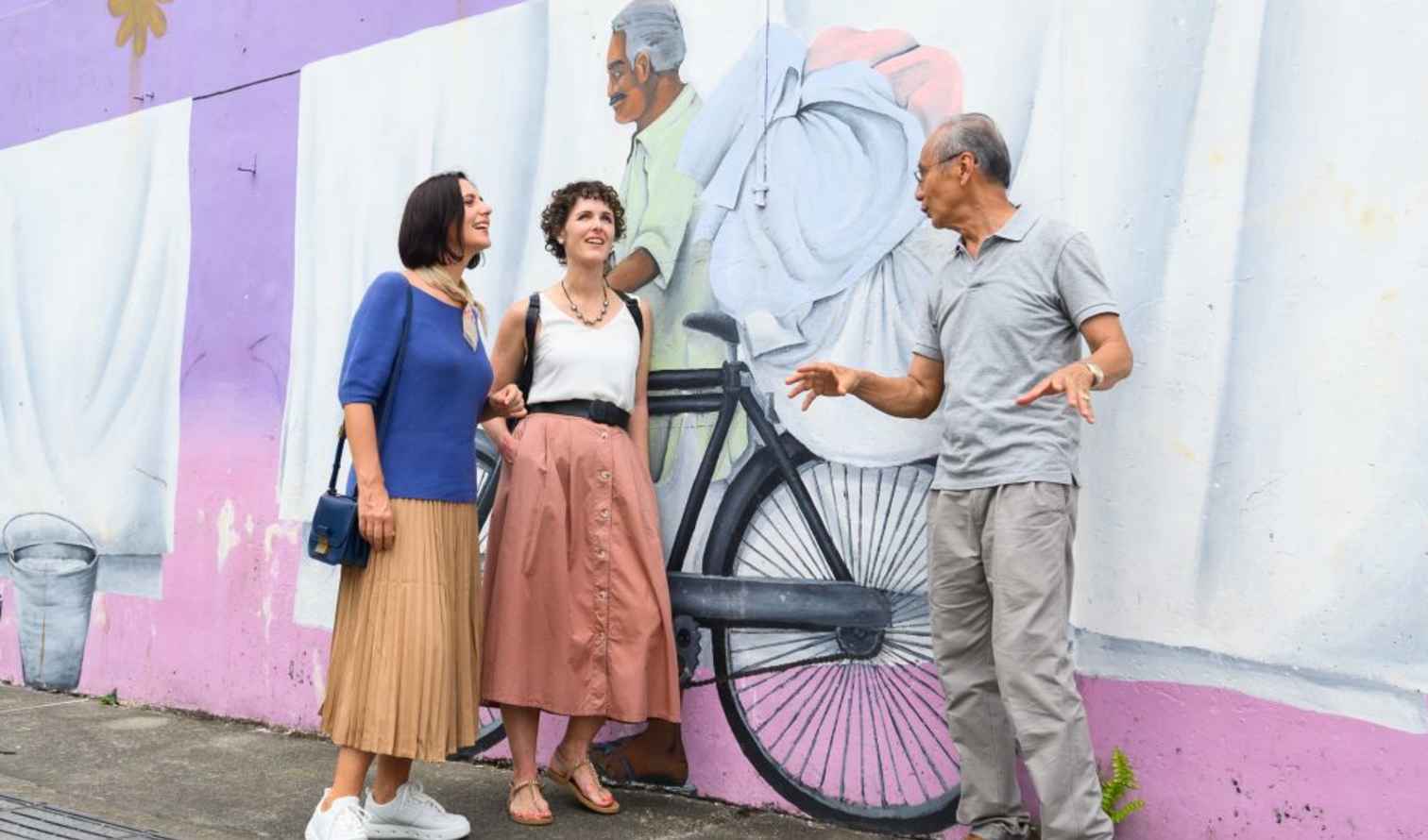 Three people standing by a mural of a bicycle rider, in Singapore