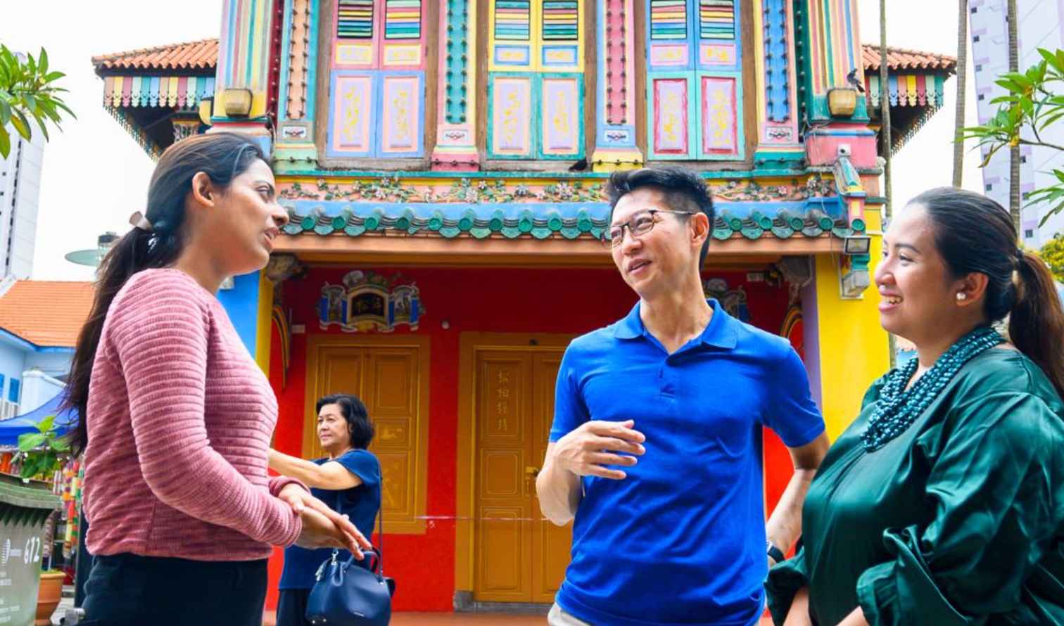 Three people talking outside the colorful Tan Teng Niah house in Singapore.