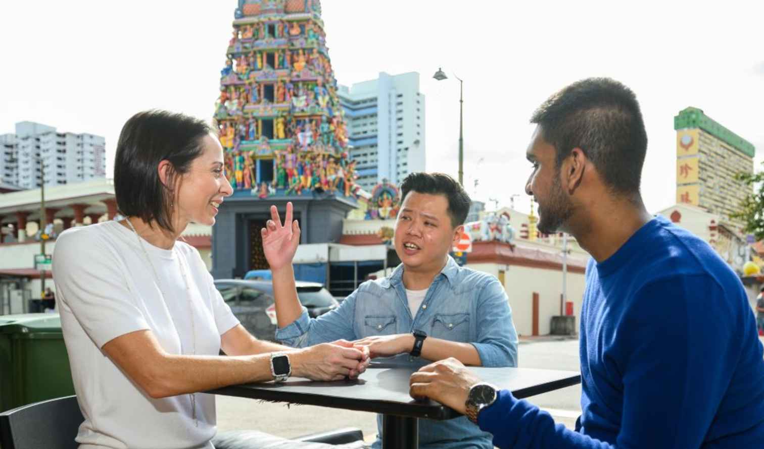 Three people seated at a table near Sri Mariamman Temple in Singapore.