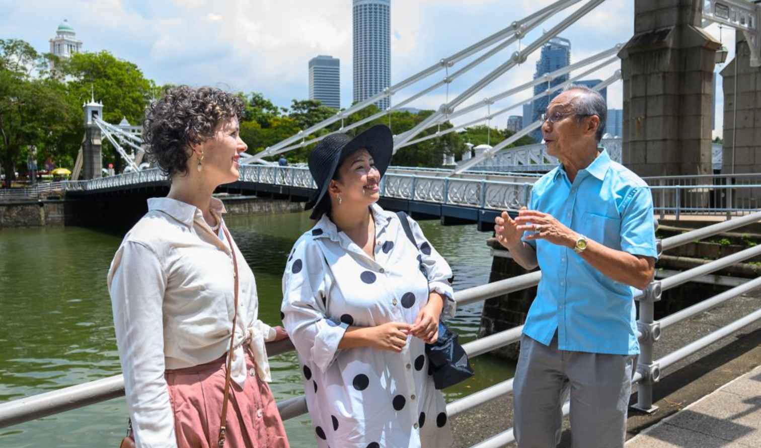 Three people talking near Cavenagh Bridge in Singapore.