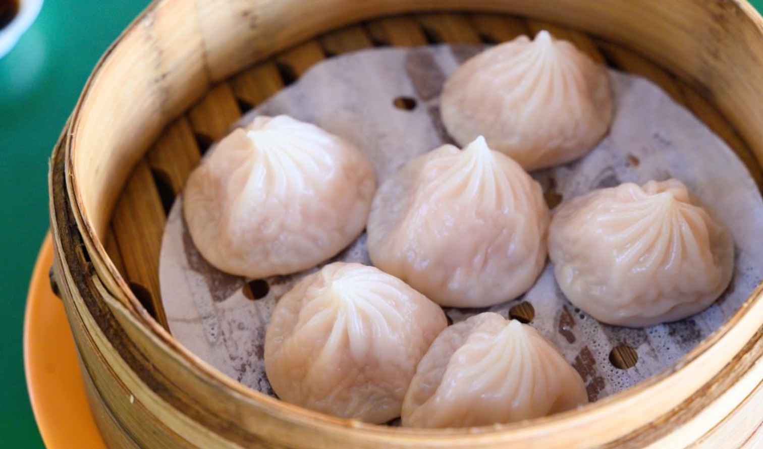 Steamed dumplings in a bamboo basket on a green table in Singapore