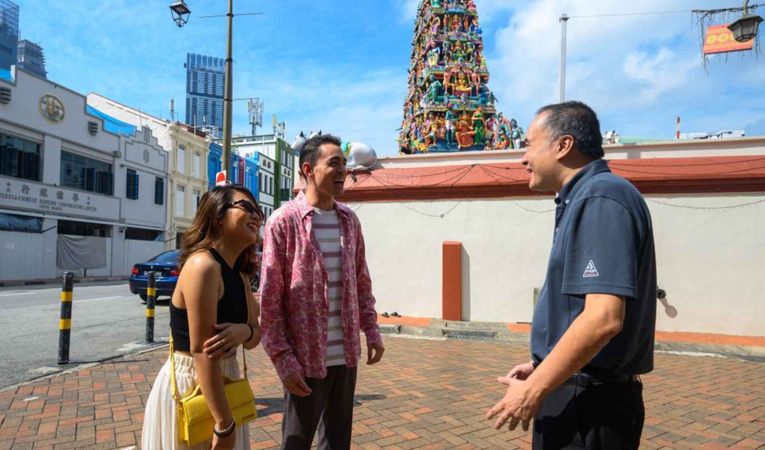 Three people talking near Sri Mariamman Temple in Singapore.