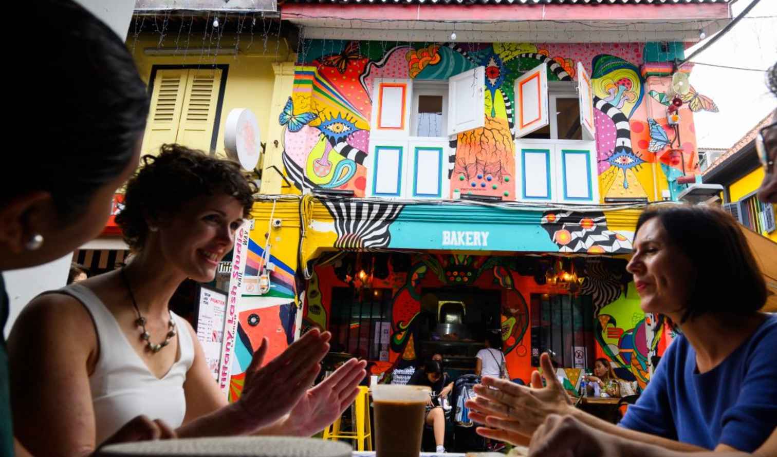 People sitting at a table in front of a colorful bakery in Haji Lane, Singapore.
