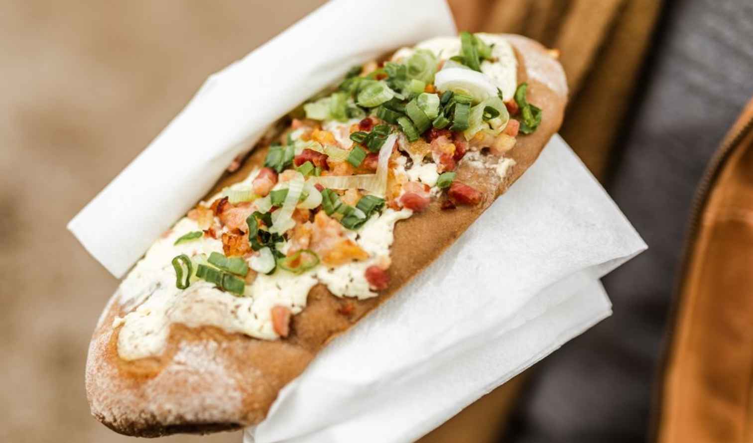 Flatbread topped with bacon, spring onions, and cream cheese held in paper wrap in Munich