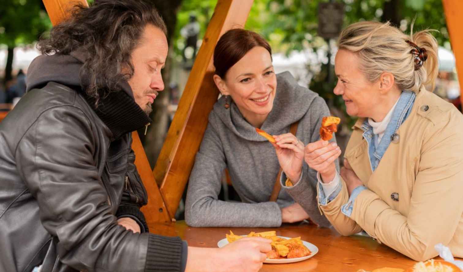 Three people sitting at a wooden table sharing a plate of food in Munich