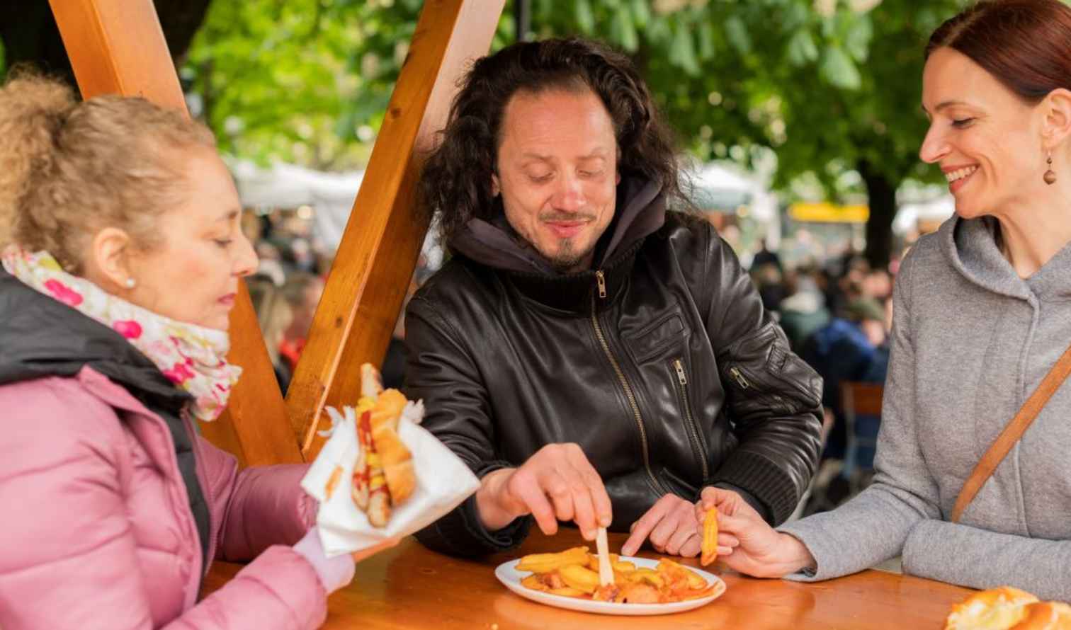 Three people eating at an outdoor market table in Munich