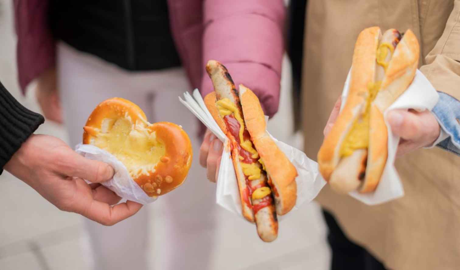 Three people holding different street foods in Munich, Germany.