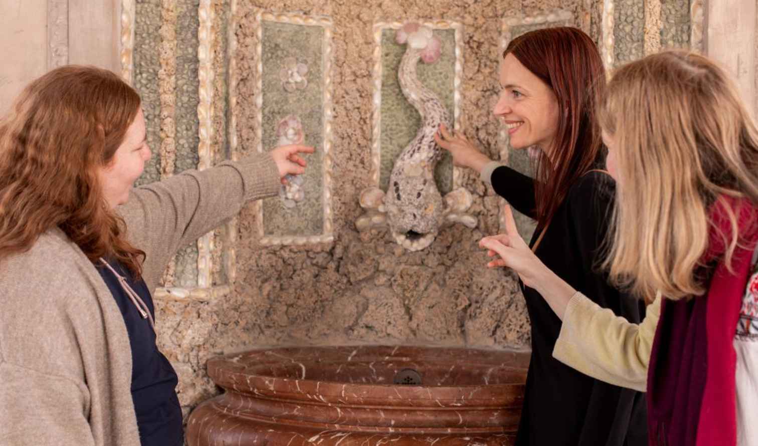 Women examining ornate stone decoration on a marbled wall installation in Munich