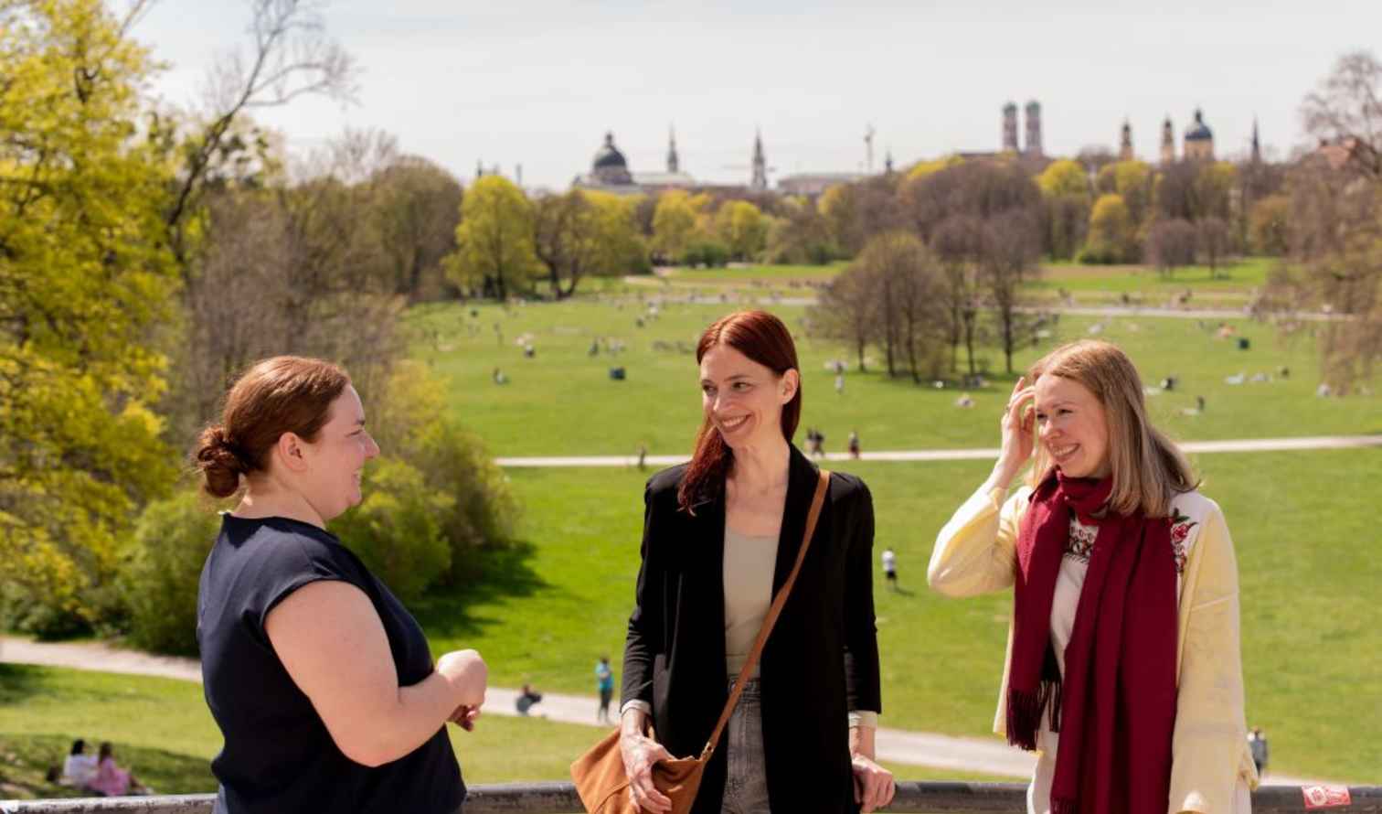 Three women talking with Munich's Englischer Garten in the background in Munich