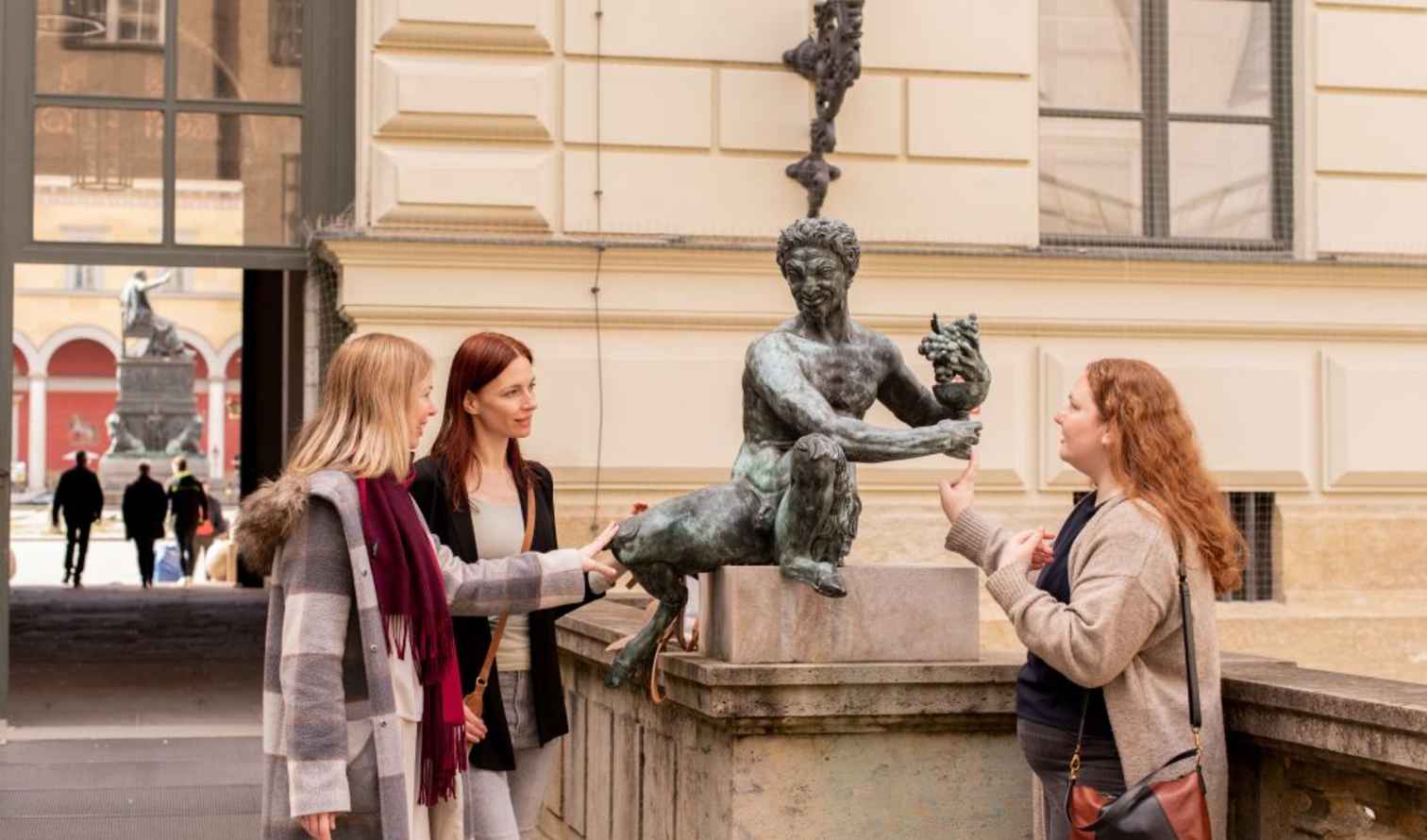 Group of women observing a statue outside a historical building in Munich.