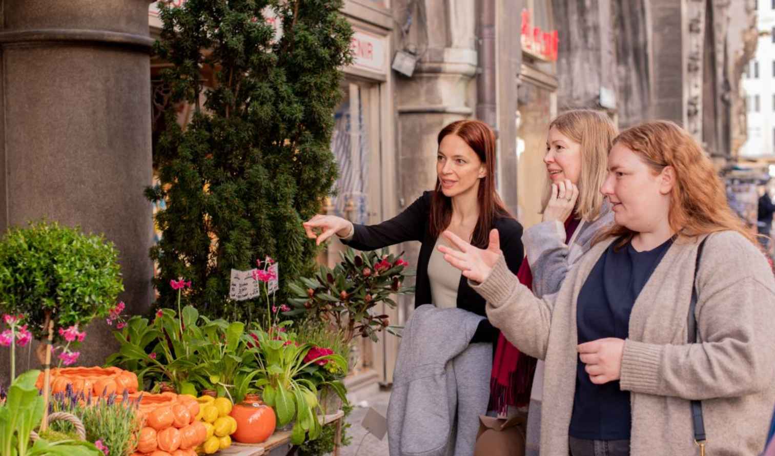 Three women looking at plants outside a flower shop in a city street in Munich