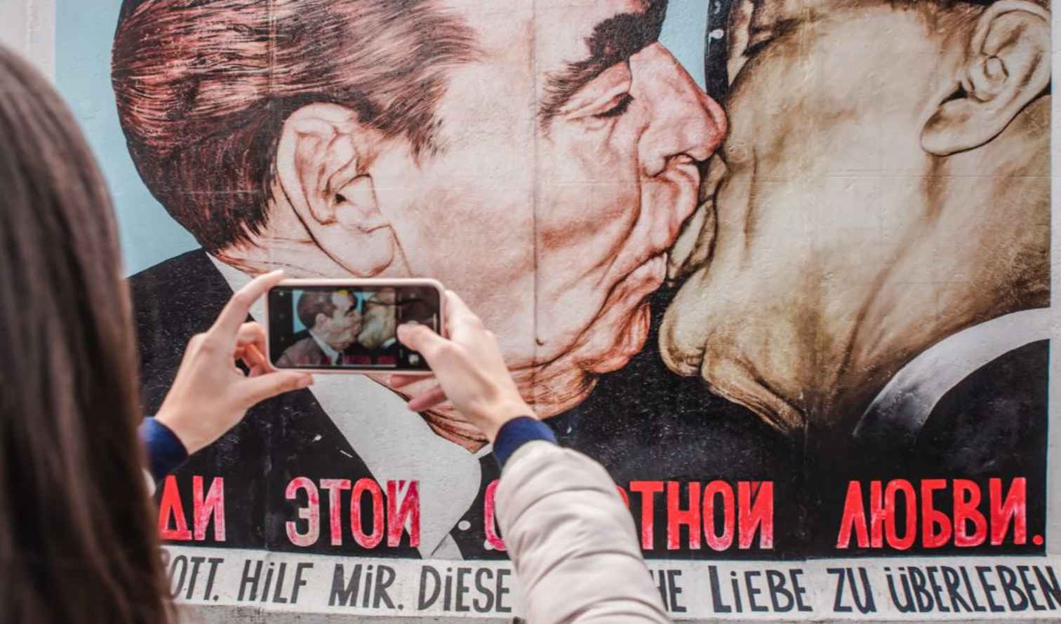 Person photographing the Berlin Wall mural of leaders kissing.