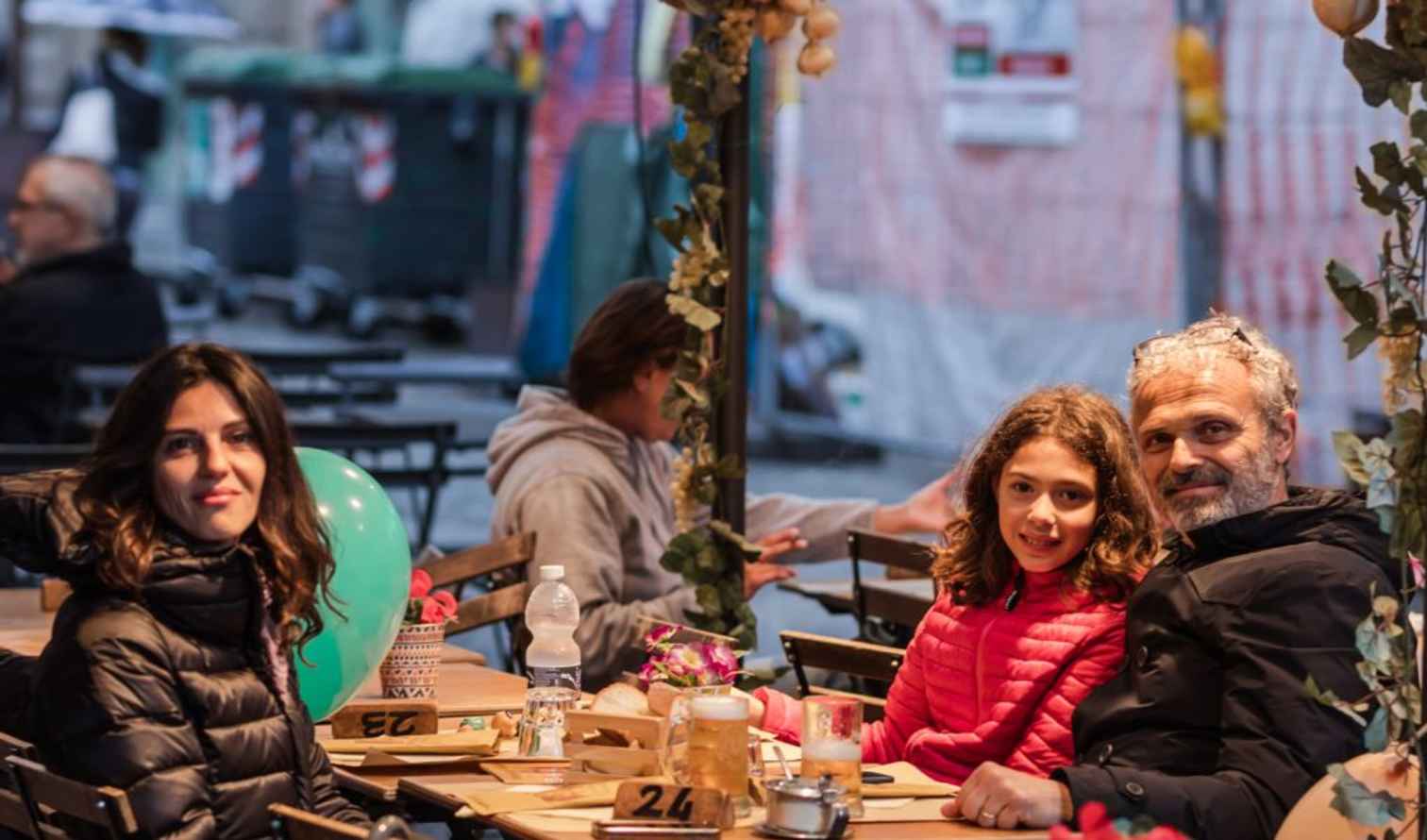 Family seated at an outdoor café table in an urban setting in Bologna