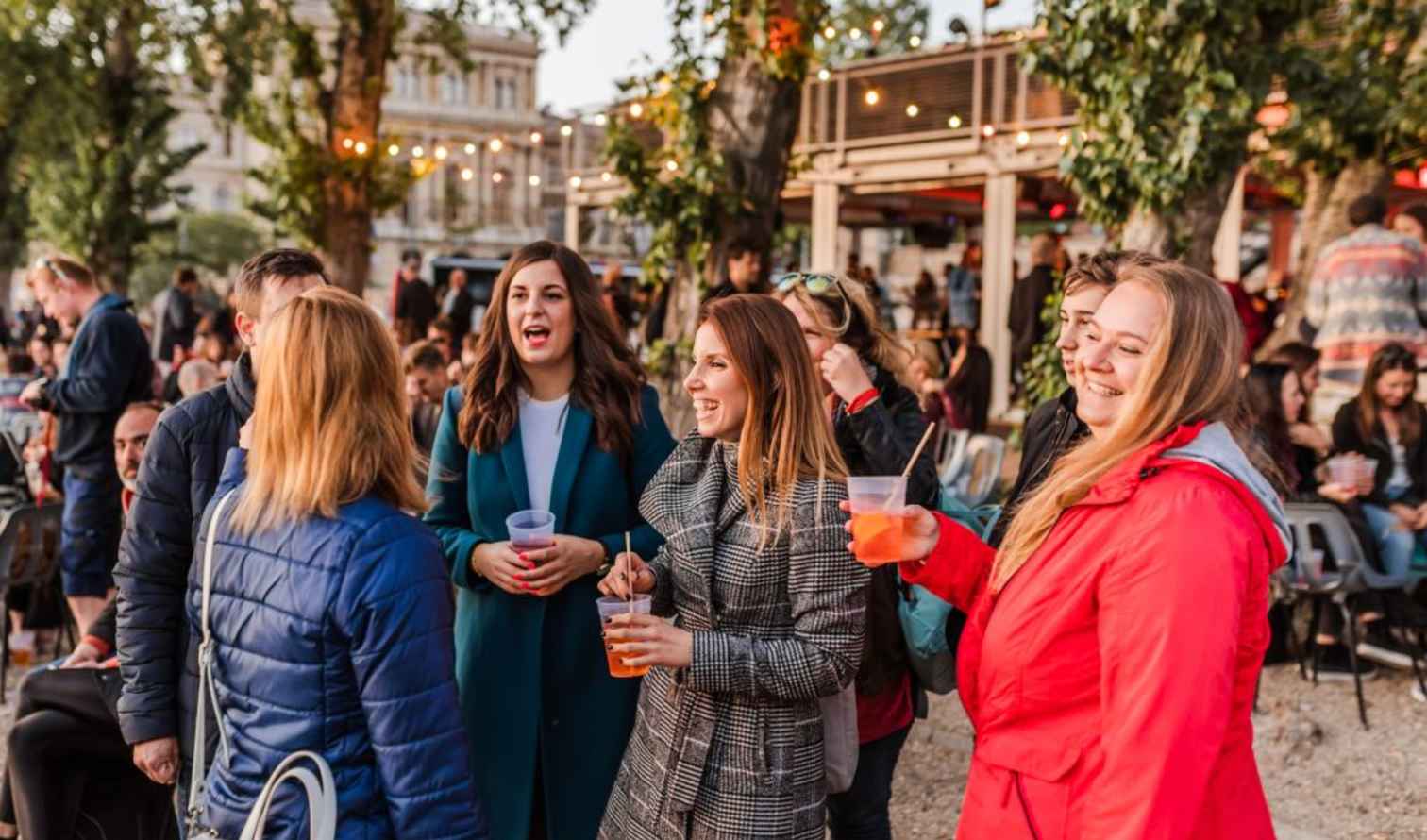 A group of people socializing in an outdoor area with trees and lights in Budapest