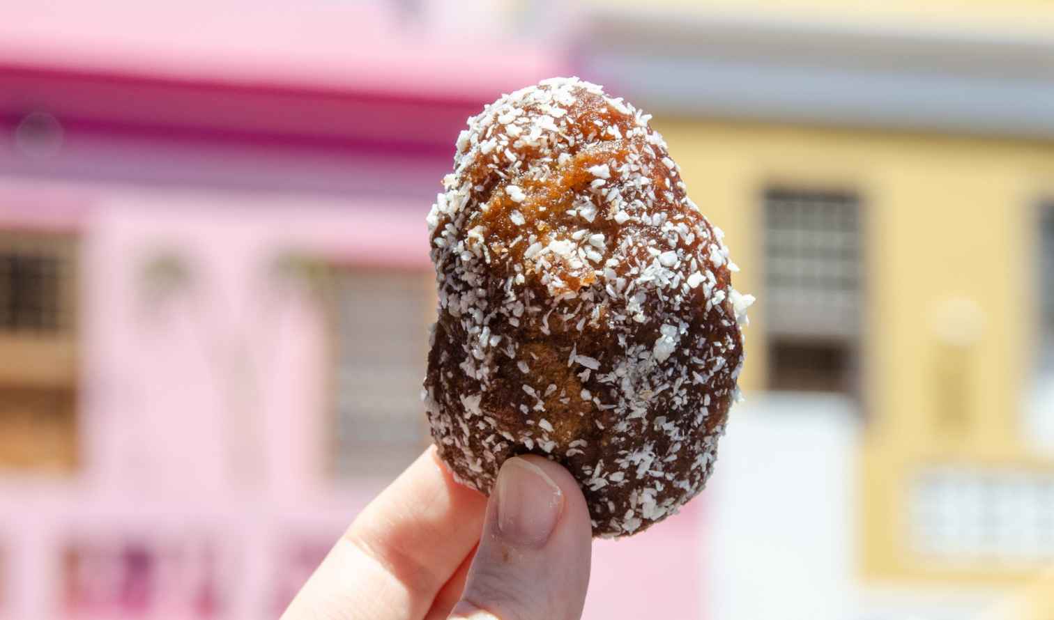 Round coconut snack held up against a blurred street background in Bo-Kaap.