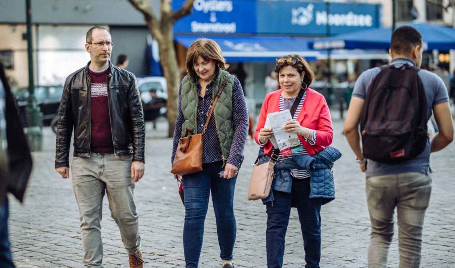 People walking on a cobblestone street near a restaurant with a blue awning in Brussels