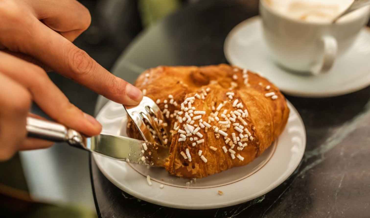 Person cutting a pastry on a plate beside a cappuccino in Brussels