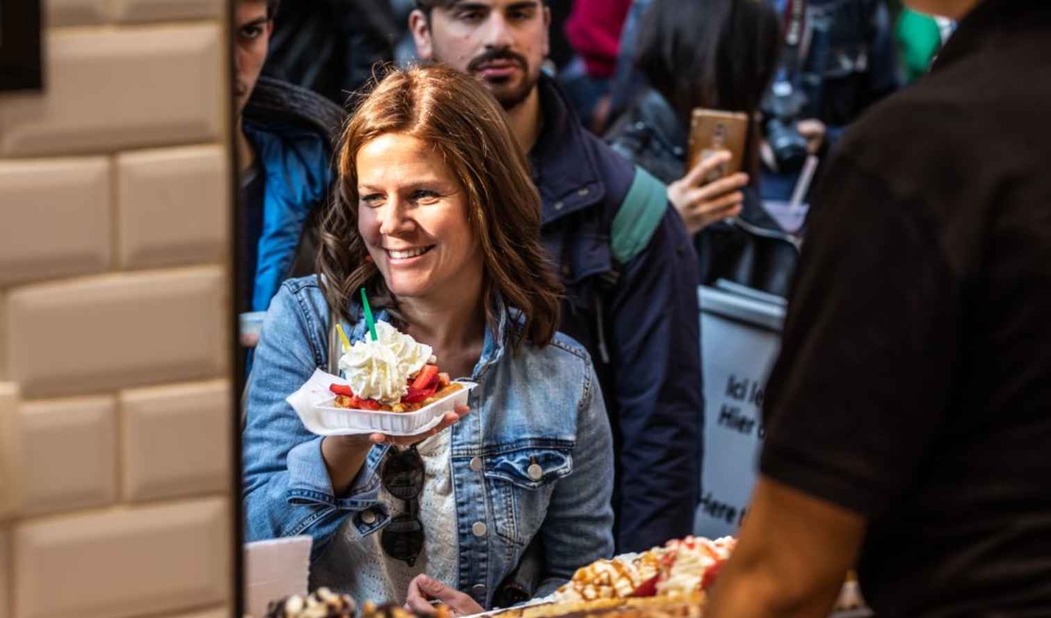 Woman holding dessert with whipped cream, standing in a crowded street market in Brussels