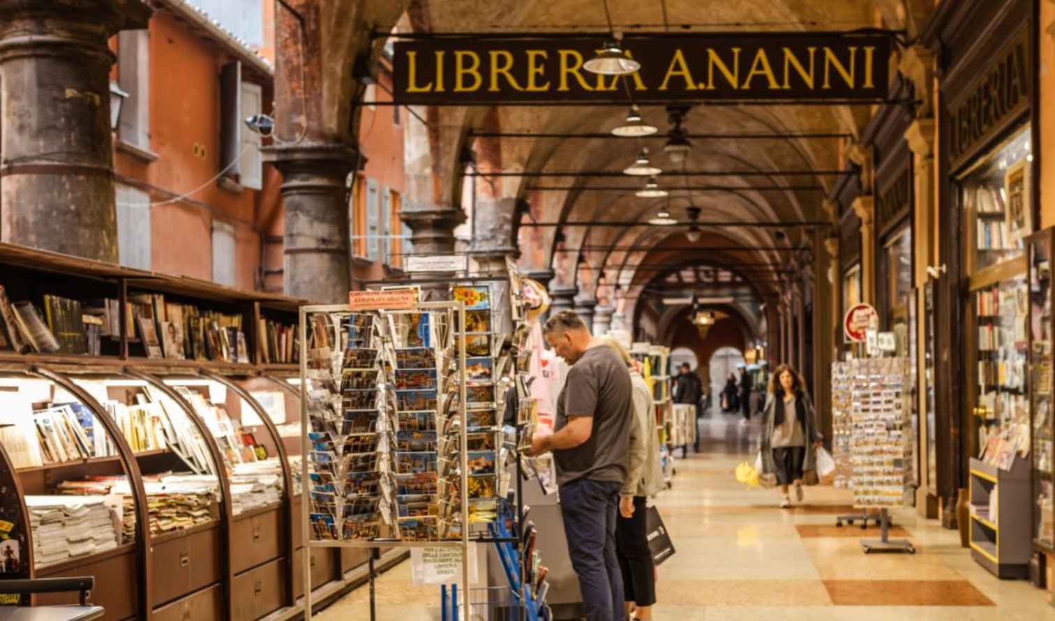 People browsing postcards under the arches of Libreria A. Nanni in Bologna.
