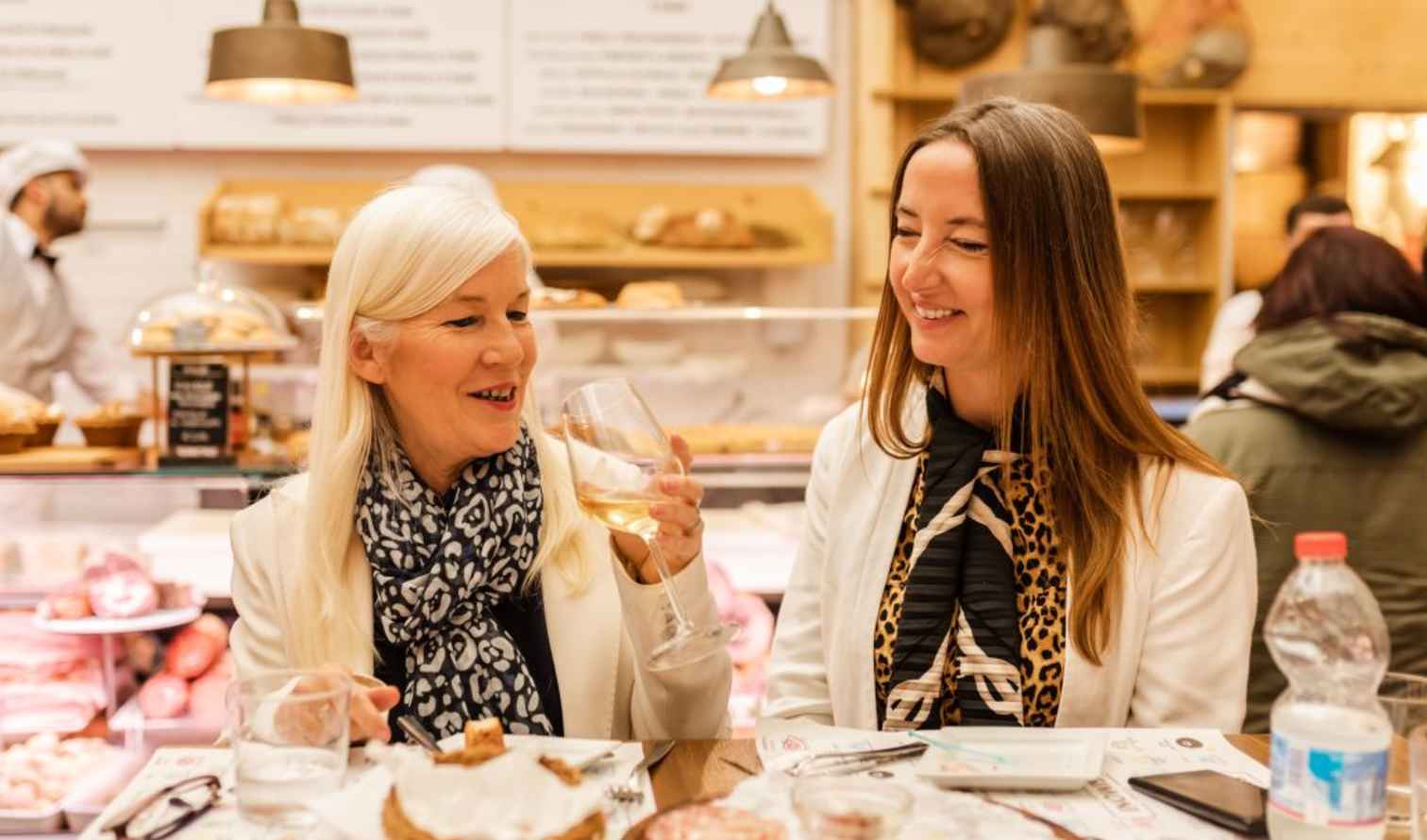 Two women seated at a deli counter enjoying wine and charcuterie  in Bologna