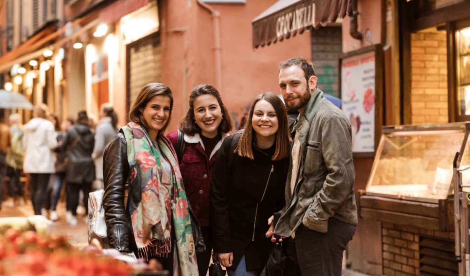 Four people standing in a street near a shop in Bologna, Italy.
