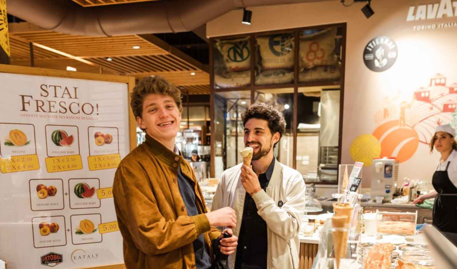 Two men stand near a signboard at Eataly, enjoying ice cream in Bologna