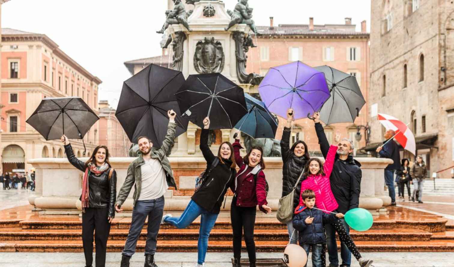 Group of people holding umbrellas in front of the Fountain of Neptune, Bologna.