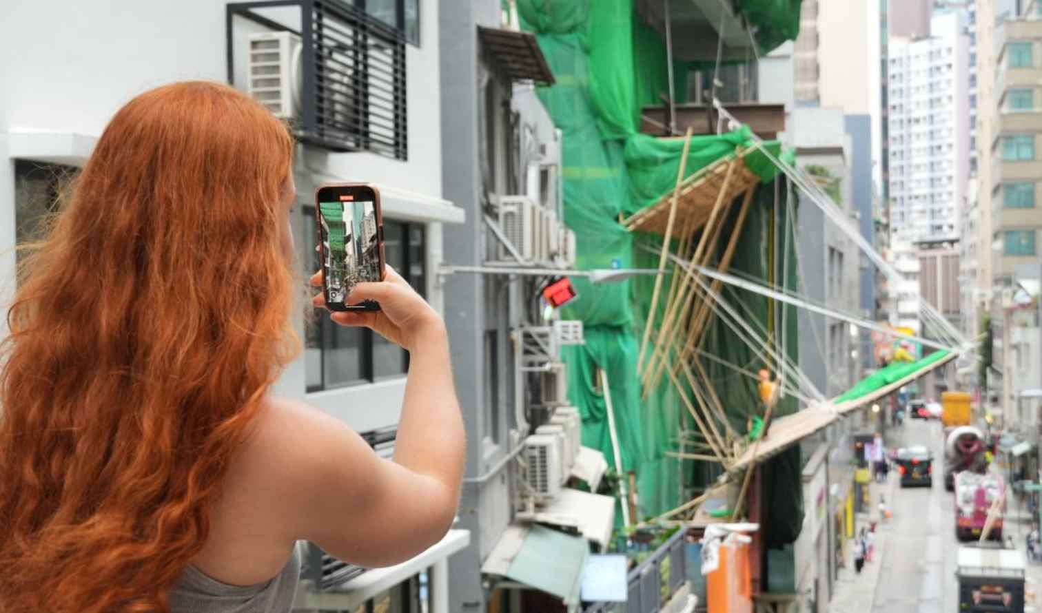 Person taking a photo of street with bamboo scaffolding in Hong Kong.