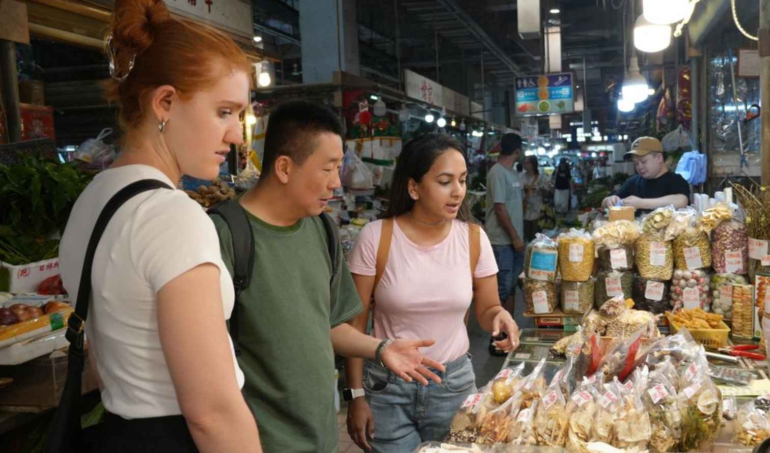 Three people examining dried goods at a market stall in Hong Kong