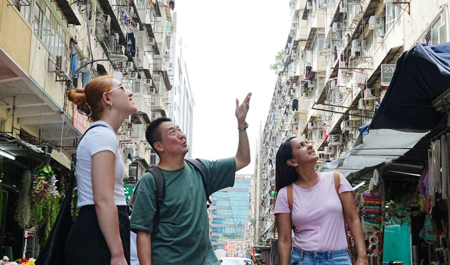 Three people look up at buildings in a narrow alley in Hong Kong.