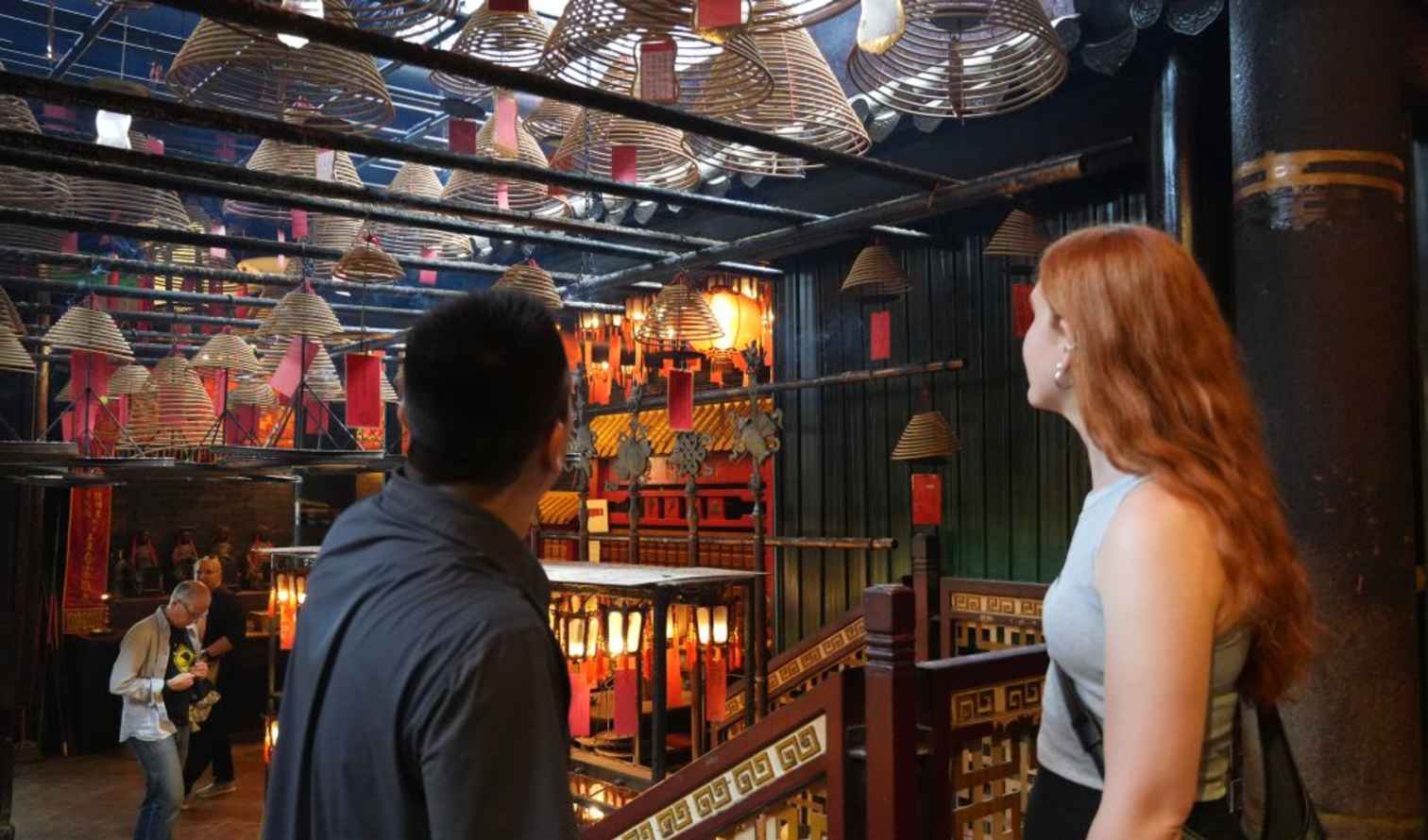Tourists explore Man Mo Temple with hanging incense spirals in Hong Kong.